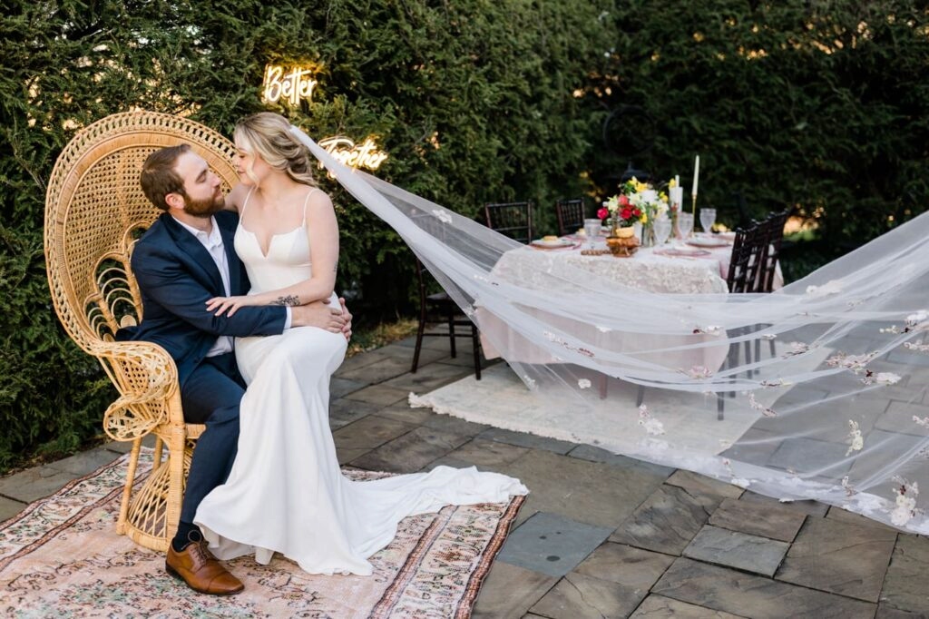 A couple snuggles on a chair beside a table at a garden wedding venue