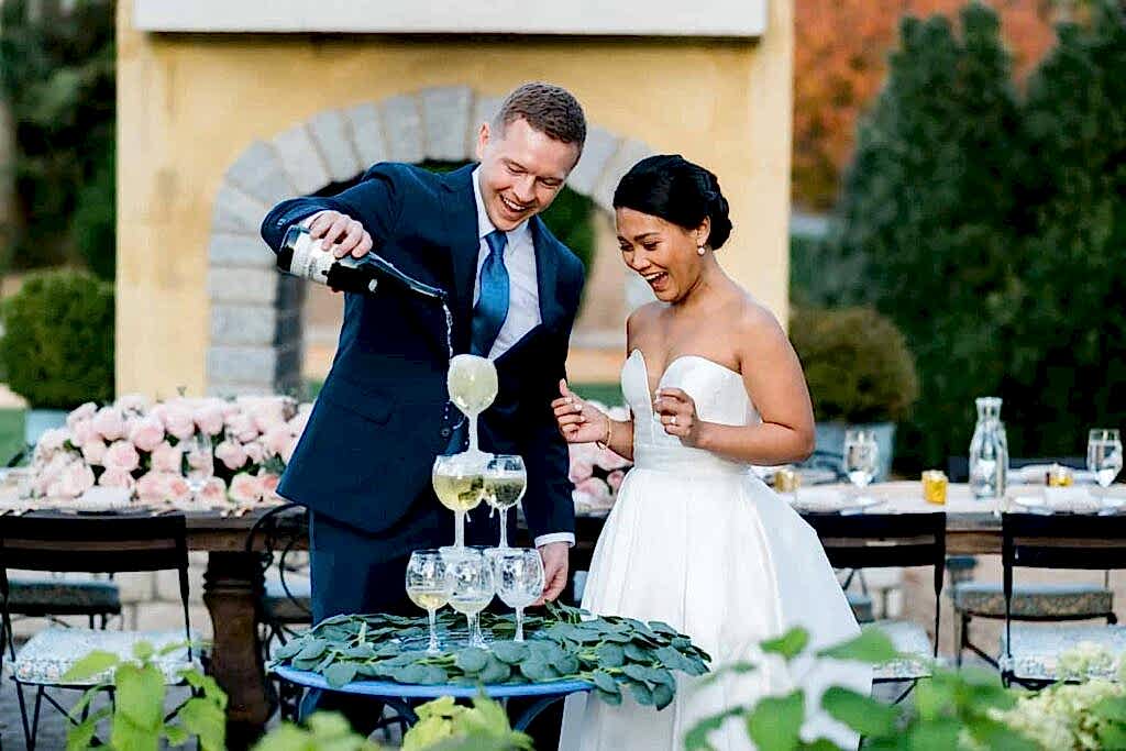 A couple pours a champagne tour during their luxury micro wedding in Charlottesville. He is holding the champagne, she is laughing