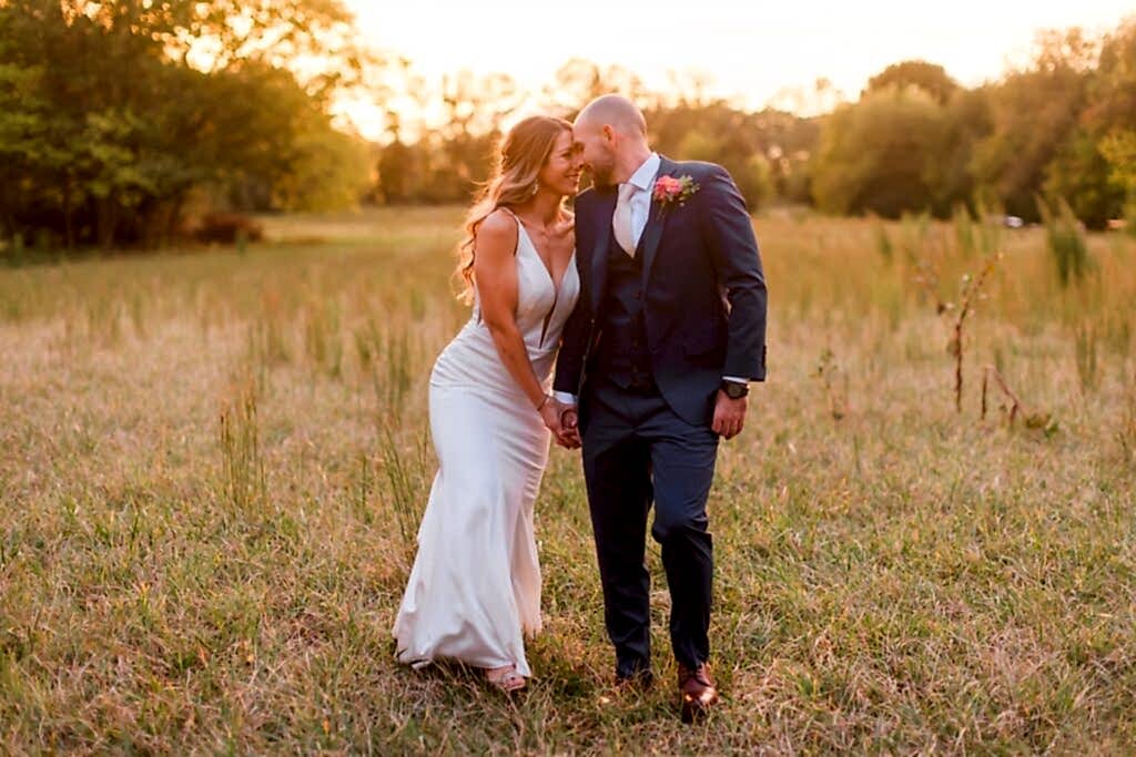 A couple nuzzles noses as they walk through a field during sunset after their wedding at Avonlea Farms