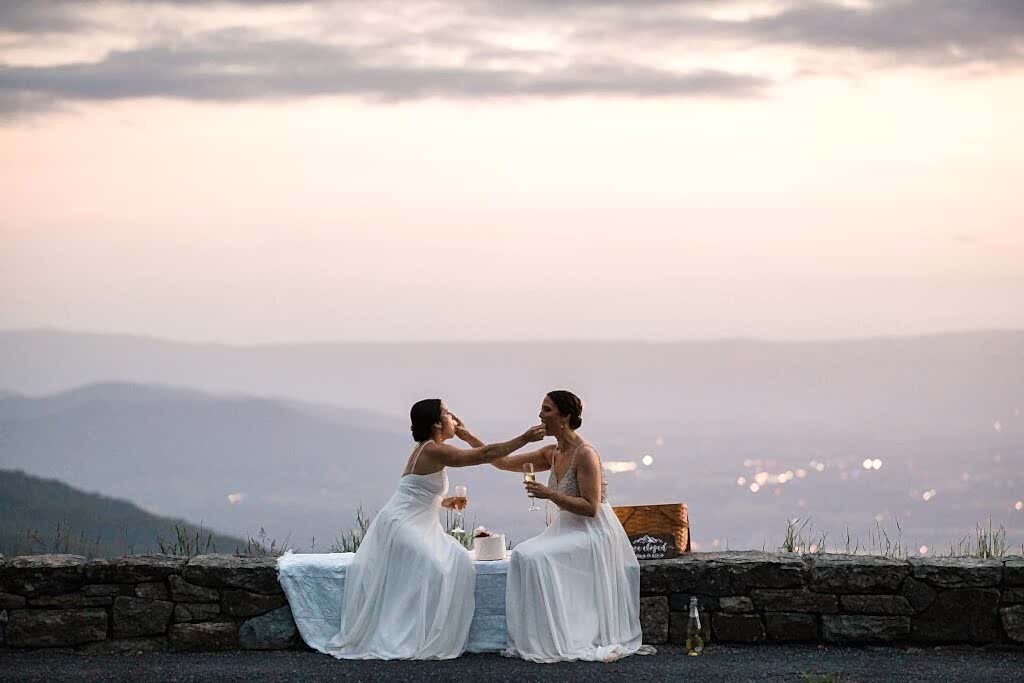 A lesbian couple celebrates their elopement in Shenandoah National Park by cutting a cake and feeding it to one another. 